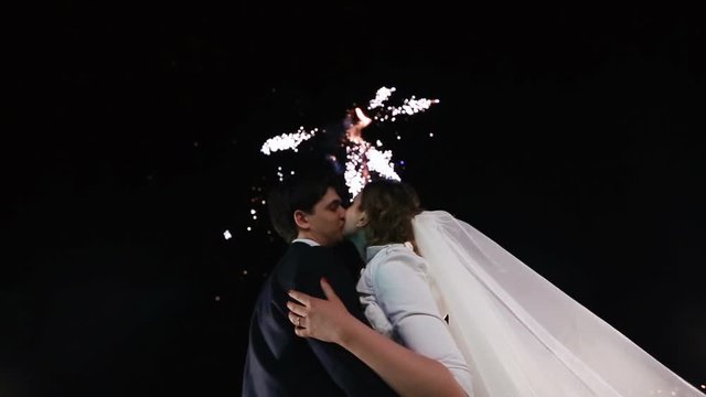Close-up portrait of the kissing newlyweds at the background of the firework.