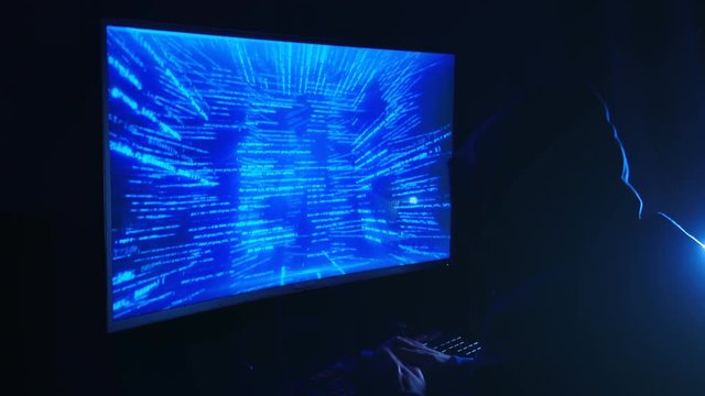 A man hacker in a hood in a dark room works with the program code