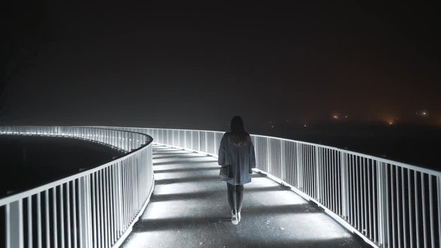 Woman walking at night on an illuminated bridge