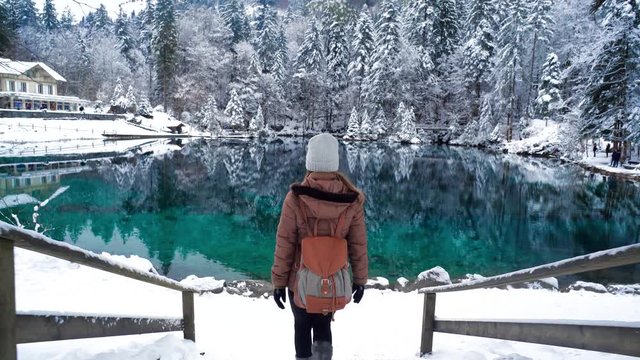 Young woman walking by frozen Blausee lake in Swiss Alps winter