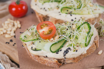 Healthy vegetarian bruschettas with bread, micro greens, hummus, cherry tomatoes, cucumbers and pine nuts