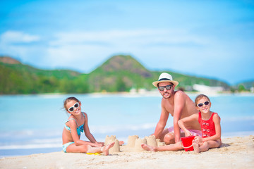 Family making sand castle at tropical white beach. Father and two girls playing with sand on tropical beach
