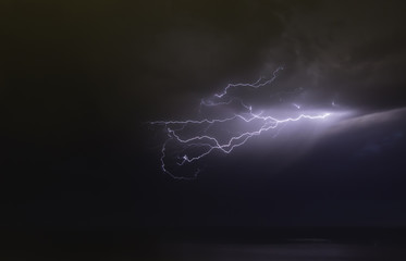 lightning bolts reflection over the sea. taken during a thunderstorm over the ocean with clouds in...