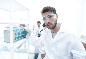Fototapeta premium Young male scientist looking at a sample in a test tube side vie