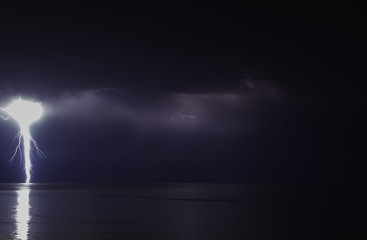 lightning bolts reflection over the sea. taken during a thunderstorm over the ocean with clouds in the background