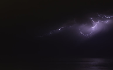 Naklejka na ściany i meble lightning bolts reflection over the sea. taken during a thunderstorm over the ocean with clouds in the background