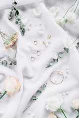Wedding composition with eucalyptus branches, bridal rings, rose flower on white textile background. Flat lay, top view festive wedding fashion concept.