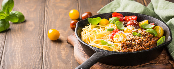 Delicious spaghetti Bolognaise or Bolognese with savory minced beef and cherry tomatoes garnished with parmesan cheese and basil in cost iron pan. Healthy italian food. Copy space. Banner.
