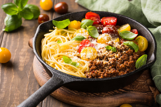 Delicious spaghetti Bolognaise or Bolognese with savory minced beef and cherry tomatoes garnished with parmesan cheese and basil in cost iron pan. Healthy italian food.