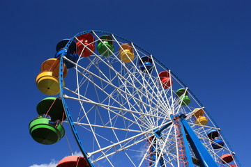Colourful Ferris Wheel over the blue clear sky with red, green, blue and yellow cabins