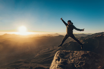 Happy man jumps joyfully on Mount Sinai on background of sunrise.