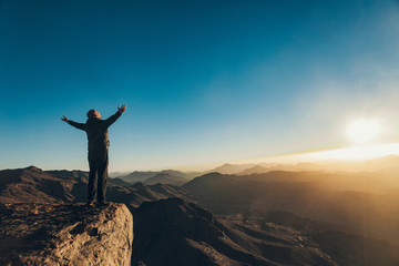 Man stands facing rising sun with lift up his arms on Mount Sinai.