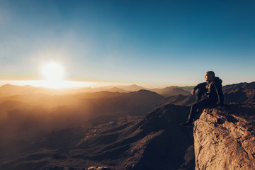 Fototapeta premium Man sits on edge of cliff on Mount Sinai against background of sunrise.
