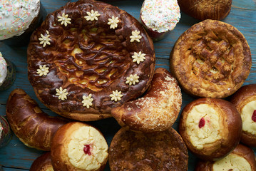 Traditional Russian Easter baked goods, kulichi, patties with cottage cheese, karavai and loaf cake with nuts on festive table background