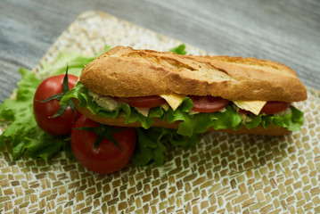 Baguette sandwich with turkey breast, cheese, lettuce, tomatoes and onion on a cutting board. Long subway sandwich on a rustic background, close-up