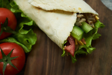 Shaurma sandwich chicken roll in a pita with fresh vegetables tomatoes , cucumber, latitude, cheese and chicken breast meat on wooden cutting board