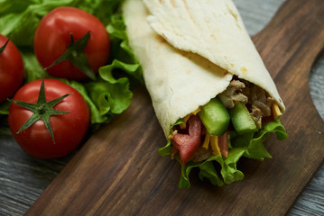 Shaurma sandwich chicken roll in a pita with fresh vegetables tomatoes , cucumber, latitude, cheese and chicken breast meat on wooden cutting board