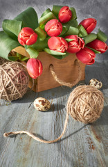Spring celebration background: bunch of red tulips, spring decorations and painted eggs on gray rustic wood