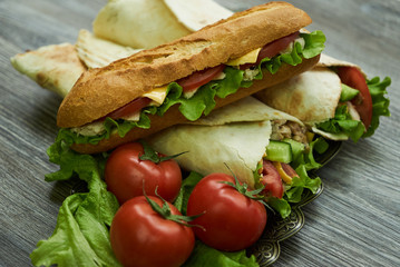 Shaurma chicken roll in a pita with fresh vegetables and long subway sandwich with tomatoes, cucumber, latitude, cheese and chicken breast fillet meat on wooden table, close-up