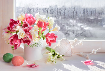 Pink tulips and white freesia flowers with Easter decorations on the window board