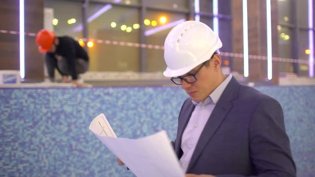 Male architector looking at the plan of building under construction. Young caucasian construction engineer looking at the building under construction. Bearded construction manager. 4 k Empty swimming