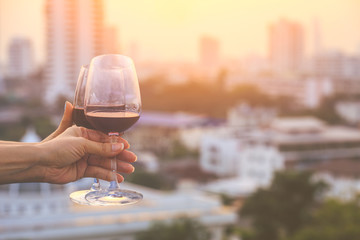close up on hands of women holding red wine glasses on balcony during sunset, celebration concept