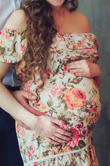 Pregnant woman in a beautiful colorful dress and her husband hugging the tummy. Pregnancy, parenthood, preparation and expectation concept