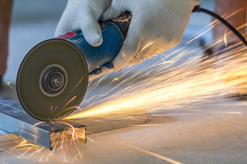 Close-up of worker cutting metal with grinder. Sparks while grinding iron.
