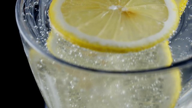 Slow motion shot of slice of lemon in soda water.