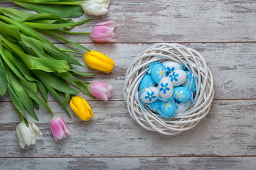 Easter eggs in a wicker basket and bouquet tulips on wooden background.Easter holiday concept.	