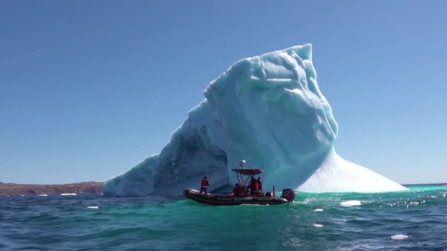 Researchers in a zodiac boat pass a massive iceberg in the Arctic.