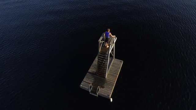 aerial young boy is scared to jump into lake from tower circling view lens flare 4k