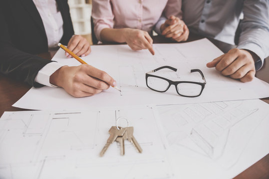 Female realtor showing contract with floor layout in an apartment to a young couple