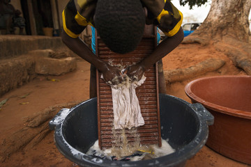 Young boy washing dirty clothes in a washing board and tub in the town of Nhacra in Guinea Bissau, West Africa - obrazy, fototapety, plakaty