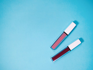 beautiful beige and red lip glosses, isolated on blue background.
