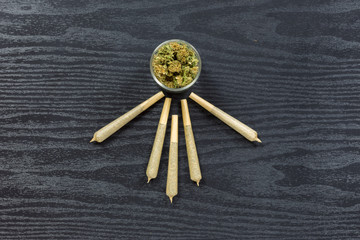 Weed in glass jar with joints arranged on black textured surface
