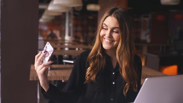 stylish young woman in black shirt sitting at cafe and taking selfie with her smart phone