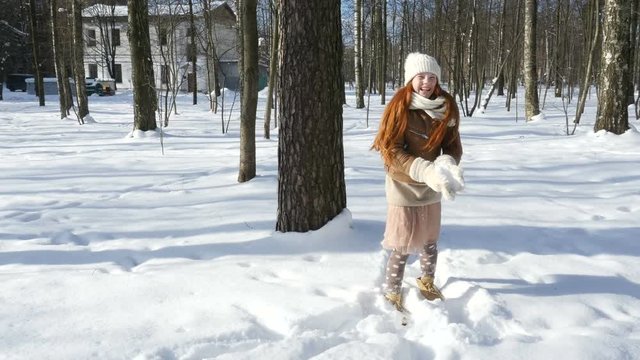 Child teenage playing on snow, red-haired girl walking at sunny winter day