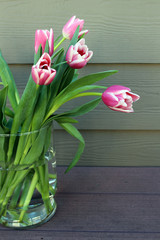 A bouquet of pink tulips in a glass vase on wooden background. Still life photography