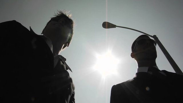A silhouetted man slyly hands another silhouetted man an envelope.