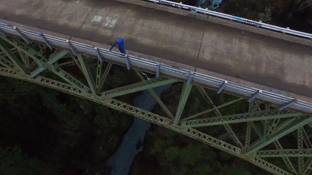 An aerial over a man standing on a steel suspension bridge over the Skokomish River in Washington, USA.