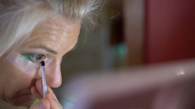 Extreme closeup of eye as a mature woman applies eye shadow with tape under her eye.