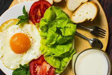 Breakfast with bread, fried eggs, milk and vegetables and fried tomato pieces on wood background