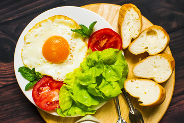Breakfast with bread, fried eggs, milk and vegetables and fried tomato pieces on wood background