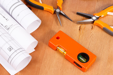 Rolls of electrical drawings or blueprints and orange work tools for use in engineer jobs lying on desk
