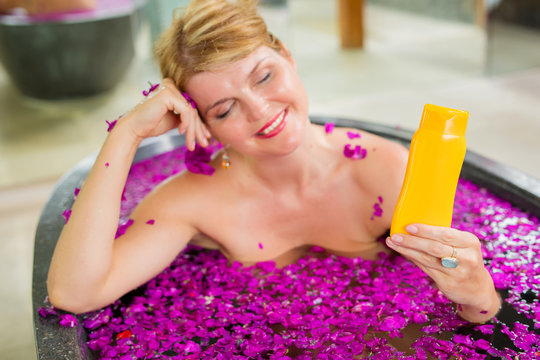 Woman showing sample beauty product bottle while sitting in bath
