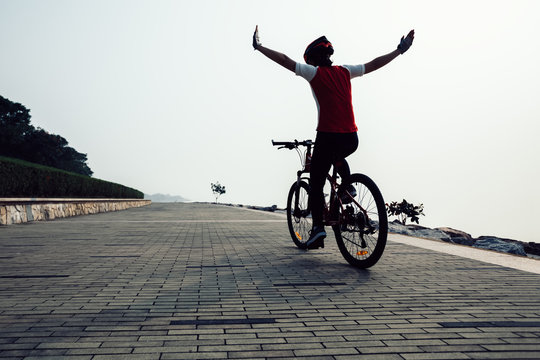 cyclist riding bike with arms outstretched in the coasts sunrise
