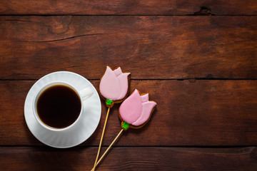 White tulips, a cup of coffee and gingerbread cookies in the shape of flowers on a dark wooden background. Concept of Spring