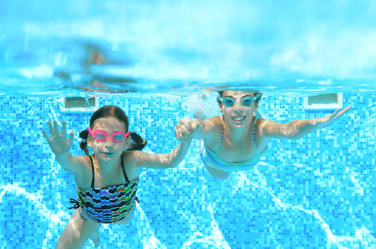 Children swim in swimming pool underwater, happy active girls have fun under water, kids fitness and sport on active family vacation
