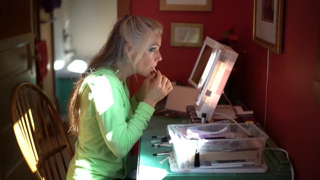 Wide shot showing setting of woman at a desk applying makeup to her eyes.